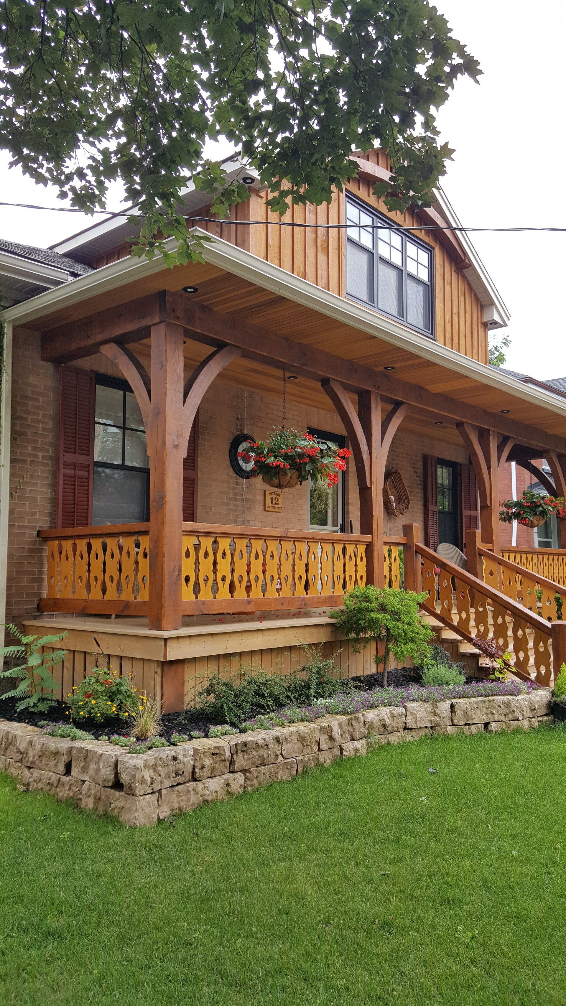 A house with a wooden timber frame porch and stairs is sitting on top of a lush green lawn.