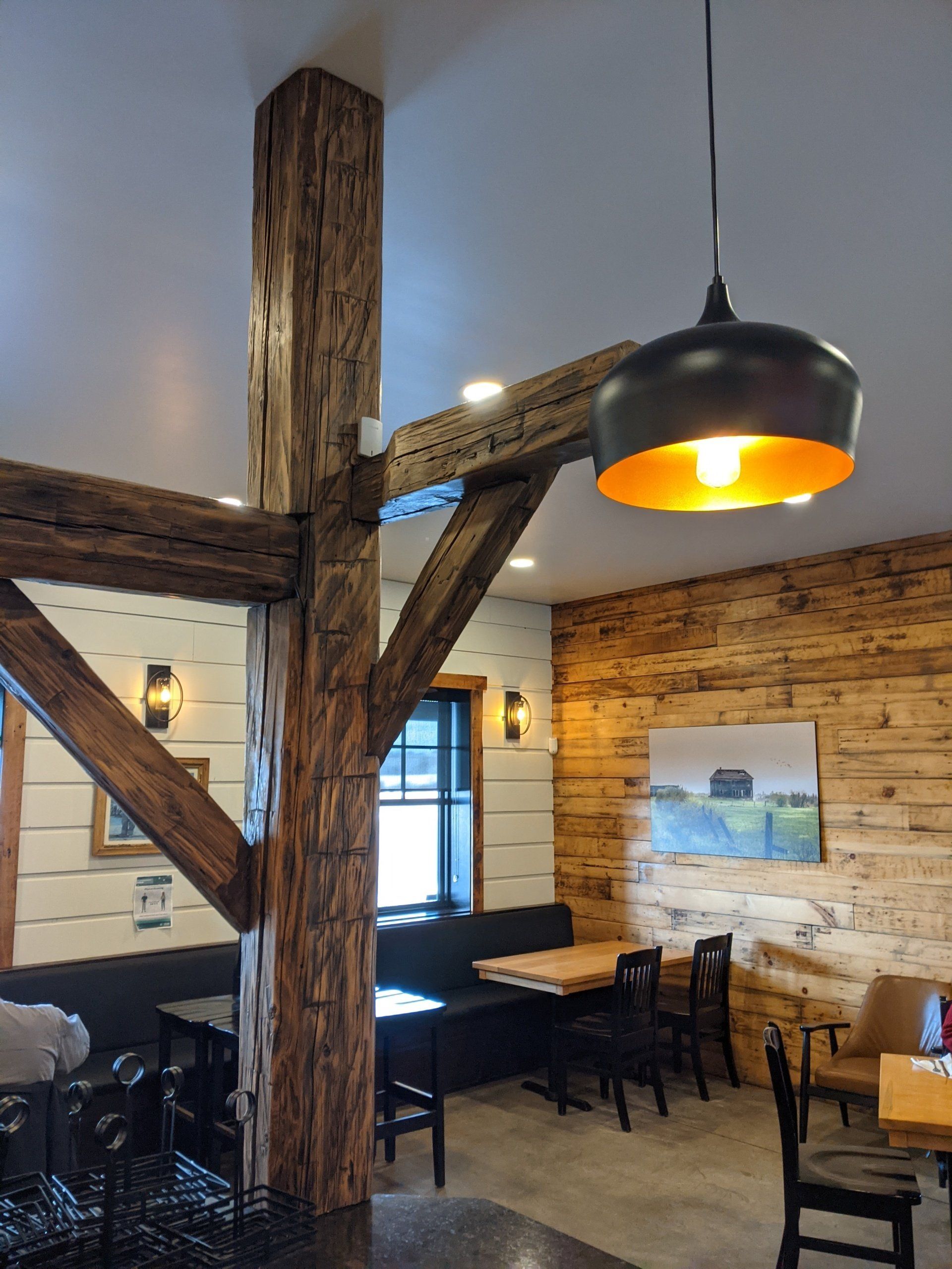 Rustic cafe interior with wood beams, black tables, chairs, and pendant light.