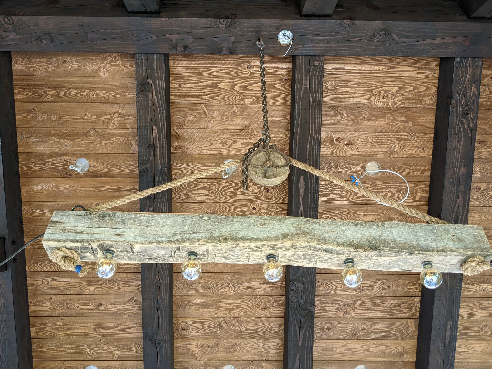 Rustic chandelier hanging from a wooden ceiling with exposed beams.