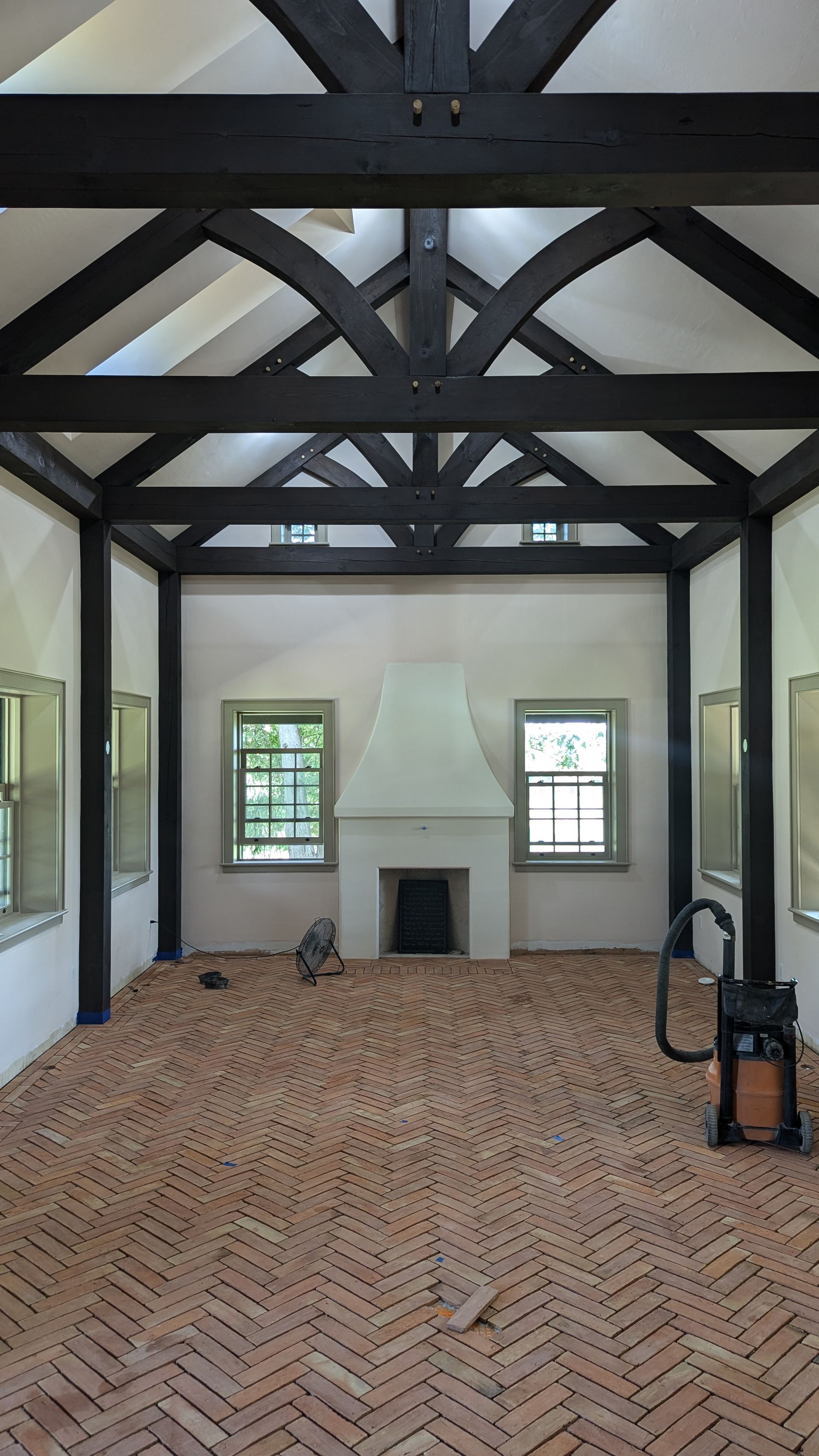 Empty room with brick floor, fireplace, and dark wood beams.