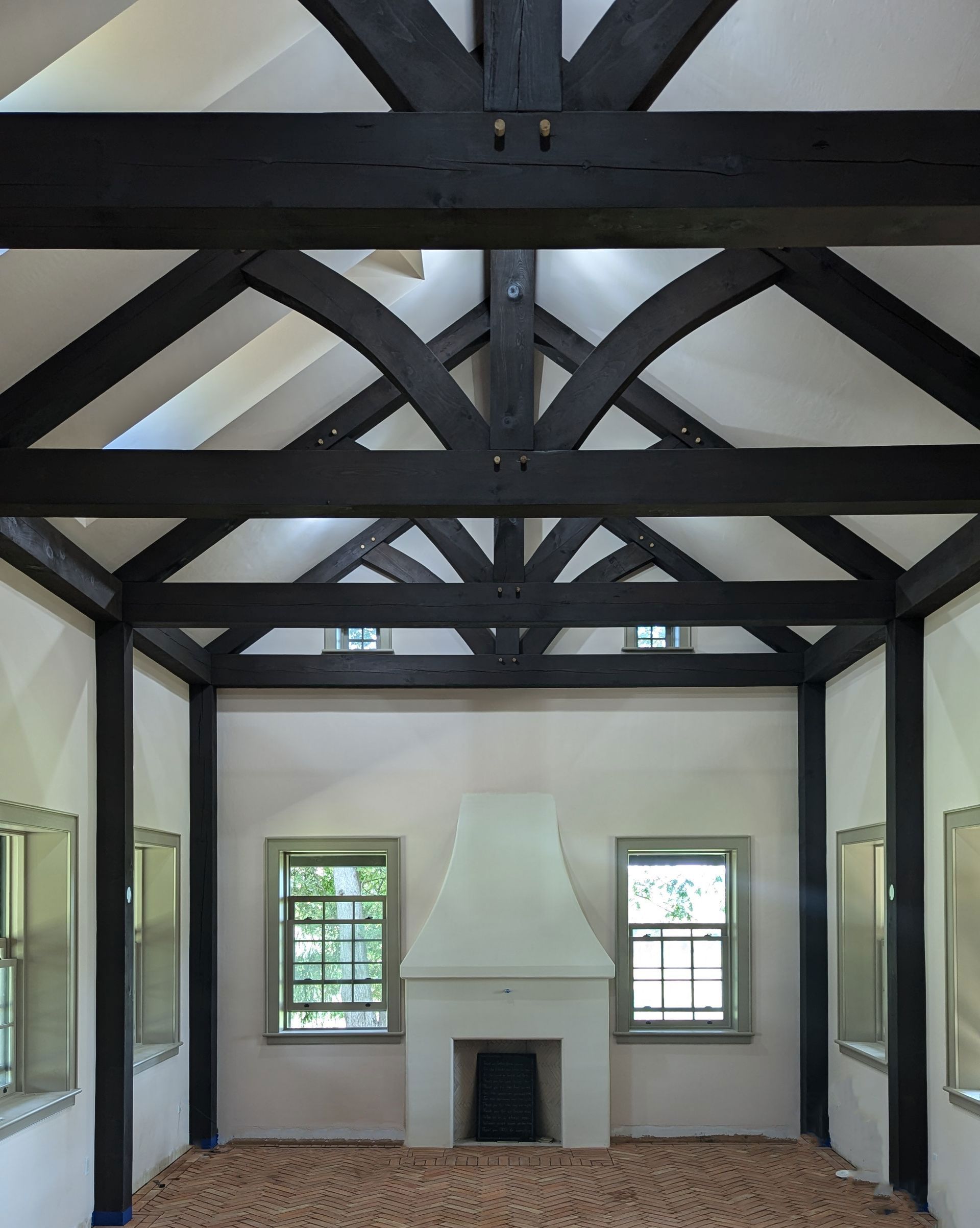 Empty room with brick floor, fireplace, and dark wood beams.
