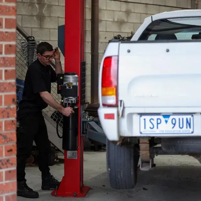 Mechanic in Black Uniform Operating a Red Vehicle Lift — COOTA Automotive Services in Ballarat East, VIC