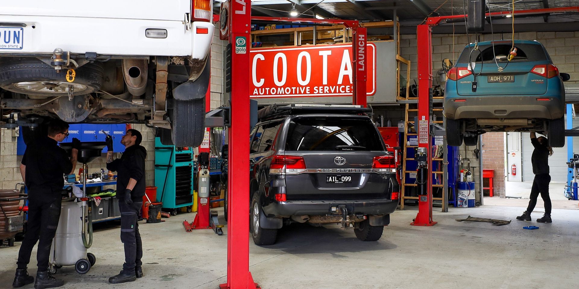 Three vehicles are being worked on in a garage. Two mechanics work on the first. A mechanic works on the third. — COOTA Automotive Services in Ballarat East, VIC