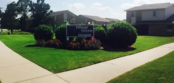 Sign with business name on it next to circular bushes — Ponca City, Oklahoma — Village Green Apartments Sign with business name on it next to circular bushes — Ponca City, Oklahoma — Village Green Apartments