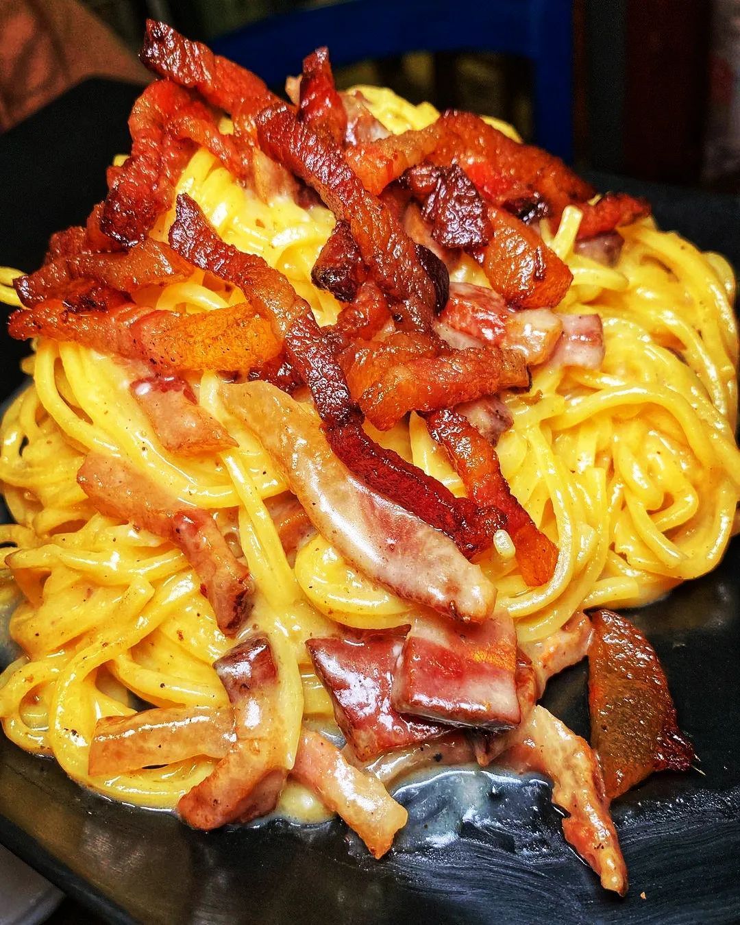 Spaghetti alla carbonara con pancetta croccante su un piatto nero.