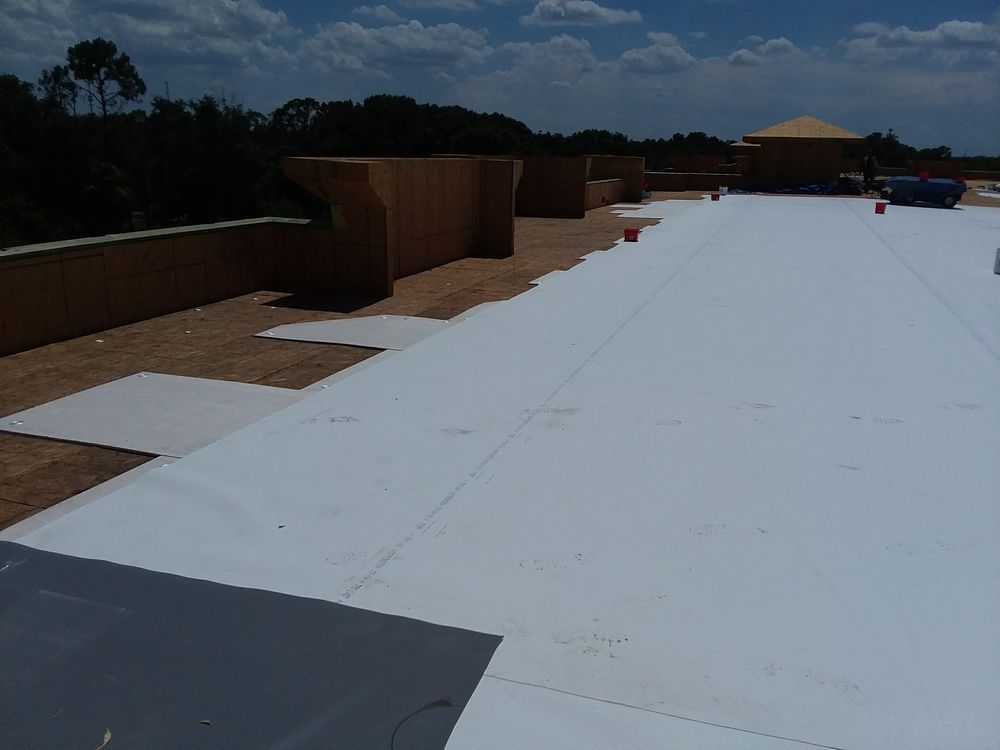 White roofing membrane being installed on a flat roof, with building materials and a blue sky.