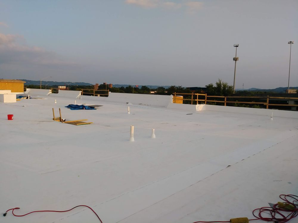 White flat roof with pipes and tools, distant trees and sky.