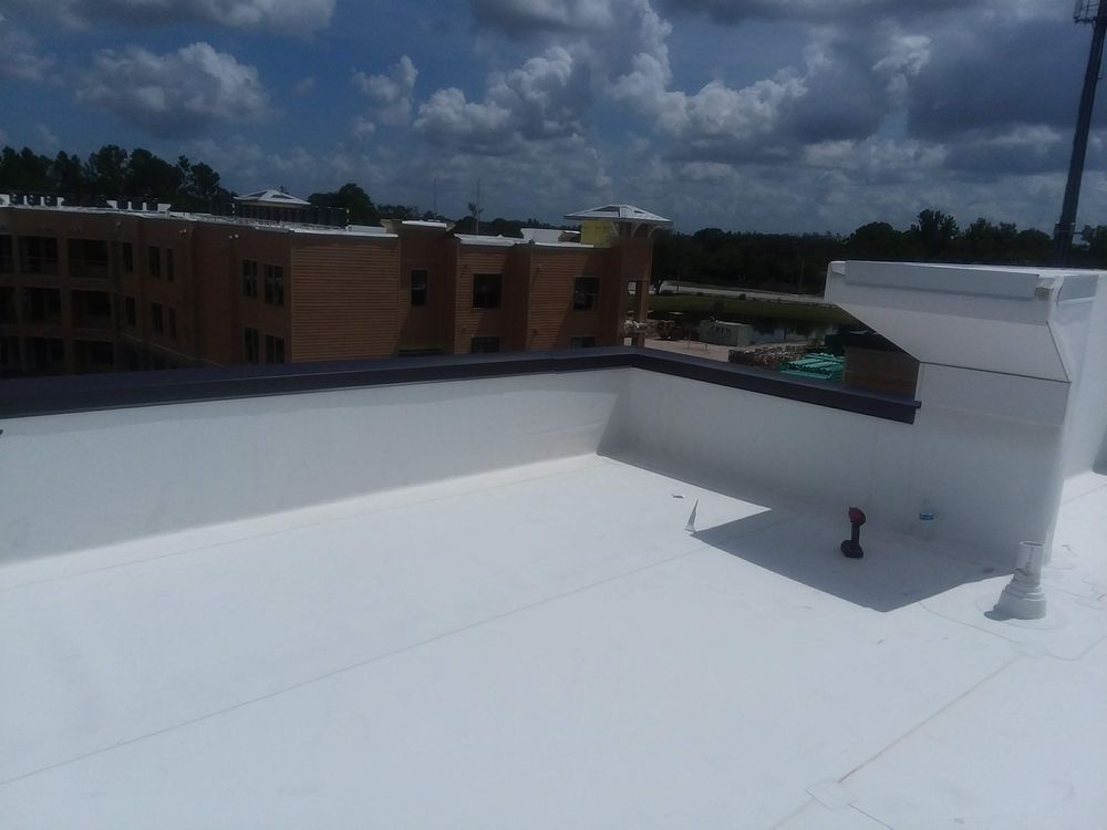 White flat roof with parapet walls and building in the background under a cloudy sky.