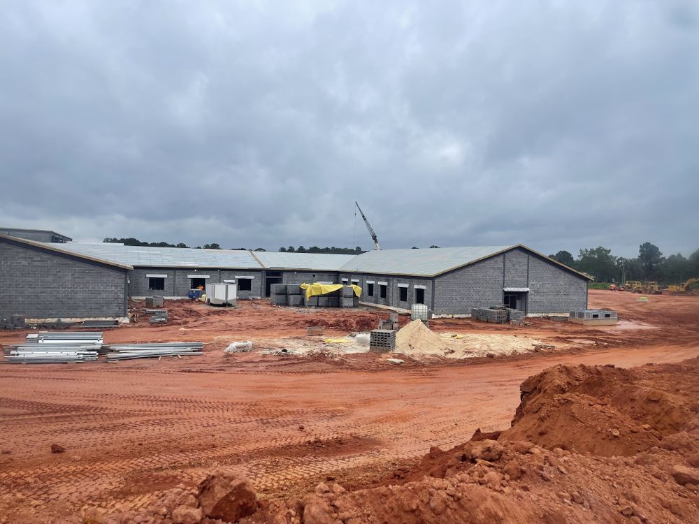 Construction site with a long, gray brick building under a cloudy sky. 