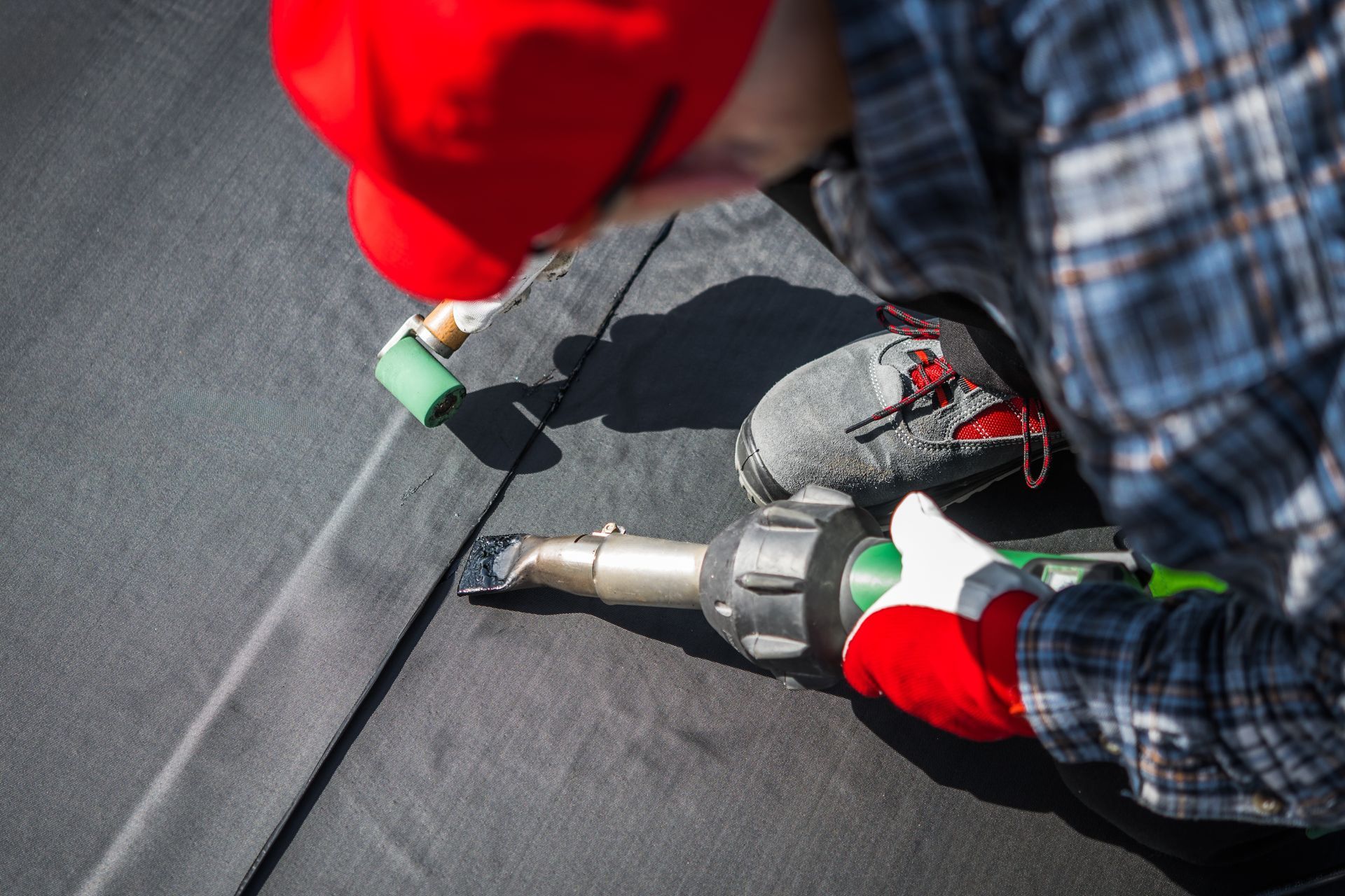 Roofer in safety gear installing metal roof panels on a building under a blue sky.