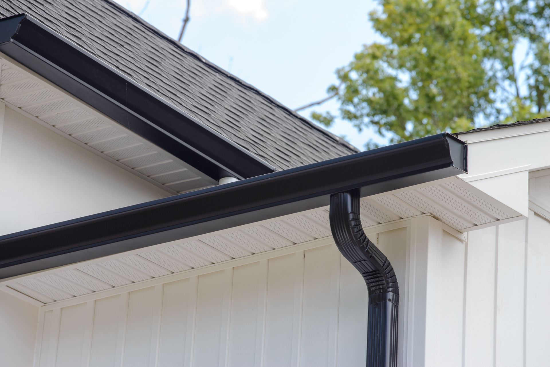 Black gutters installed on a white house, with a dark gray roof.