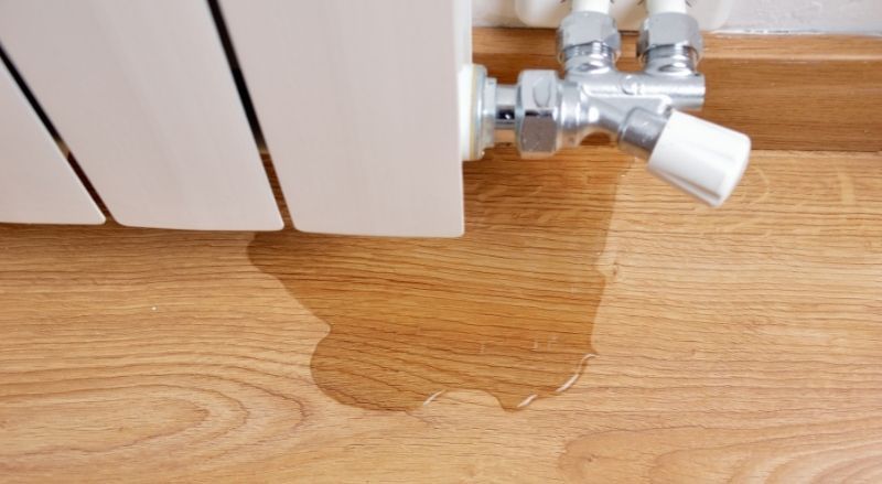 Un radiateur fuit de l'eau sur un plancher en bois.