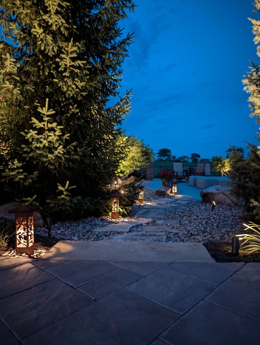 Technician inspecting landscape lighting fixture at dusk