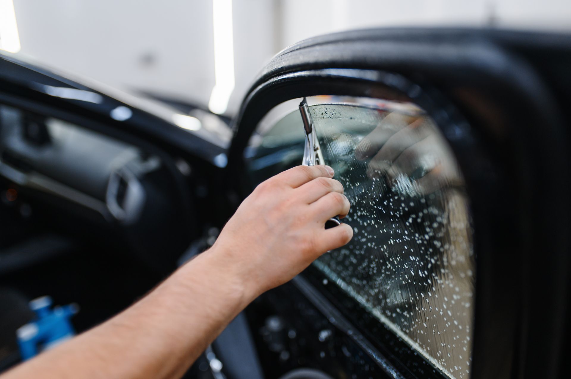 A person is applying tinted window film to a car window.