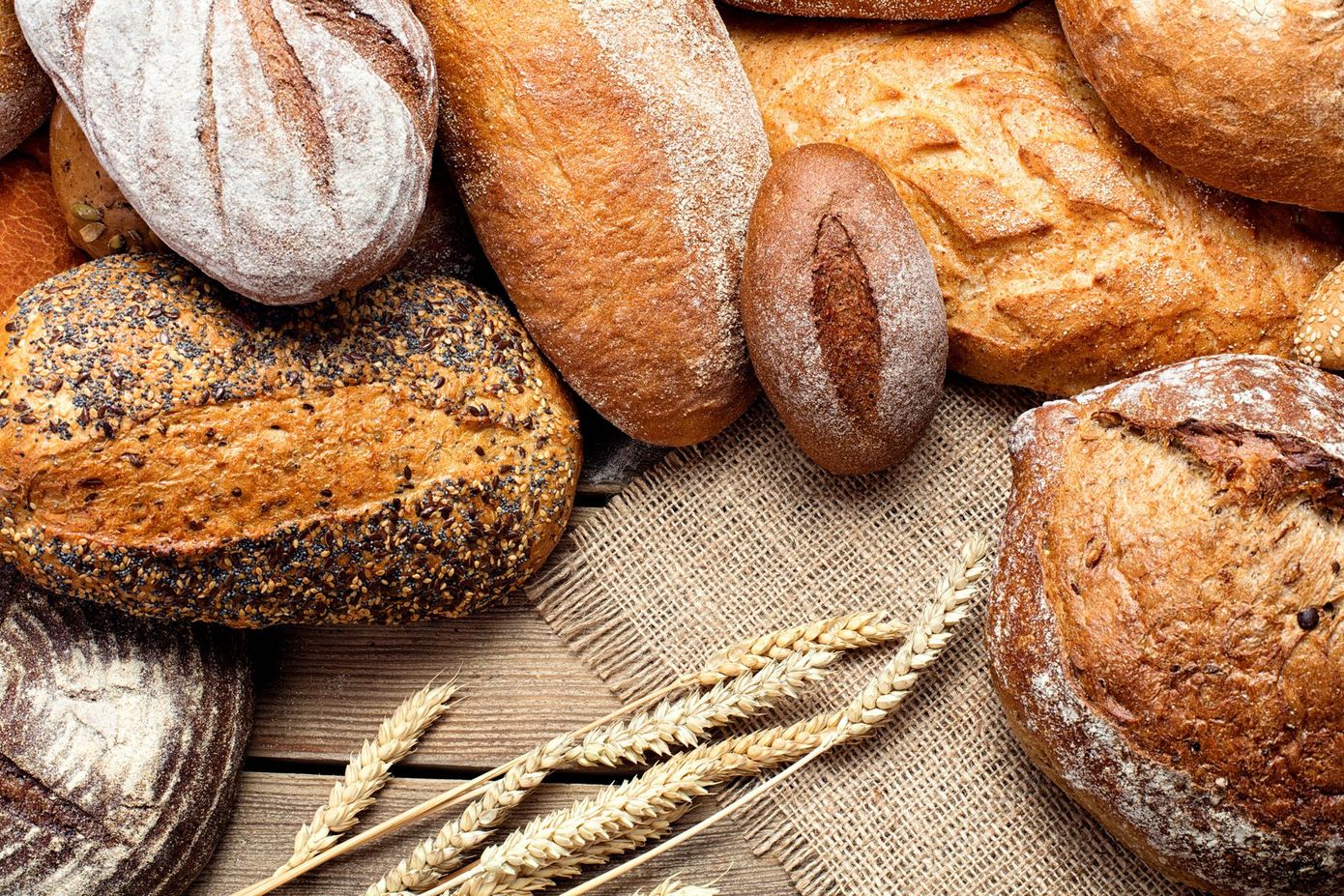 Assortimento di pagnotte e baguette rustiche su tela di iuta con steli di grano.
