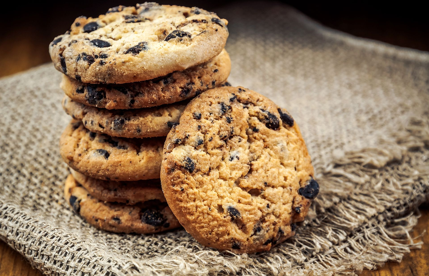 Pila di biscotti con gocce di cioccolato su un telo di iuta, con un biscotto che sporge in avanti.
