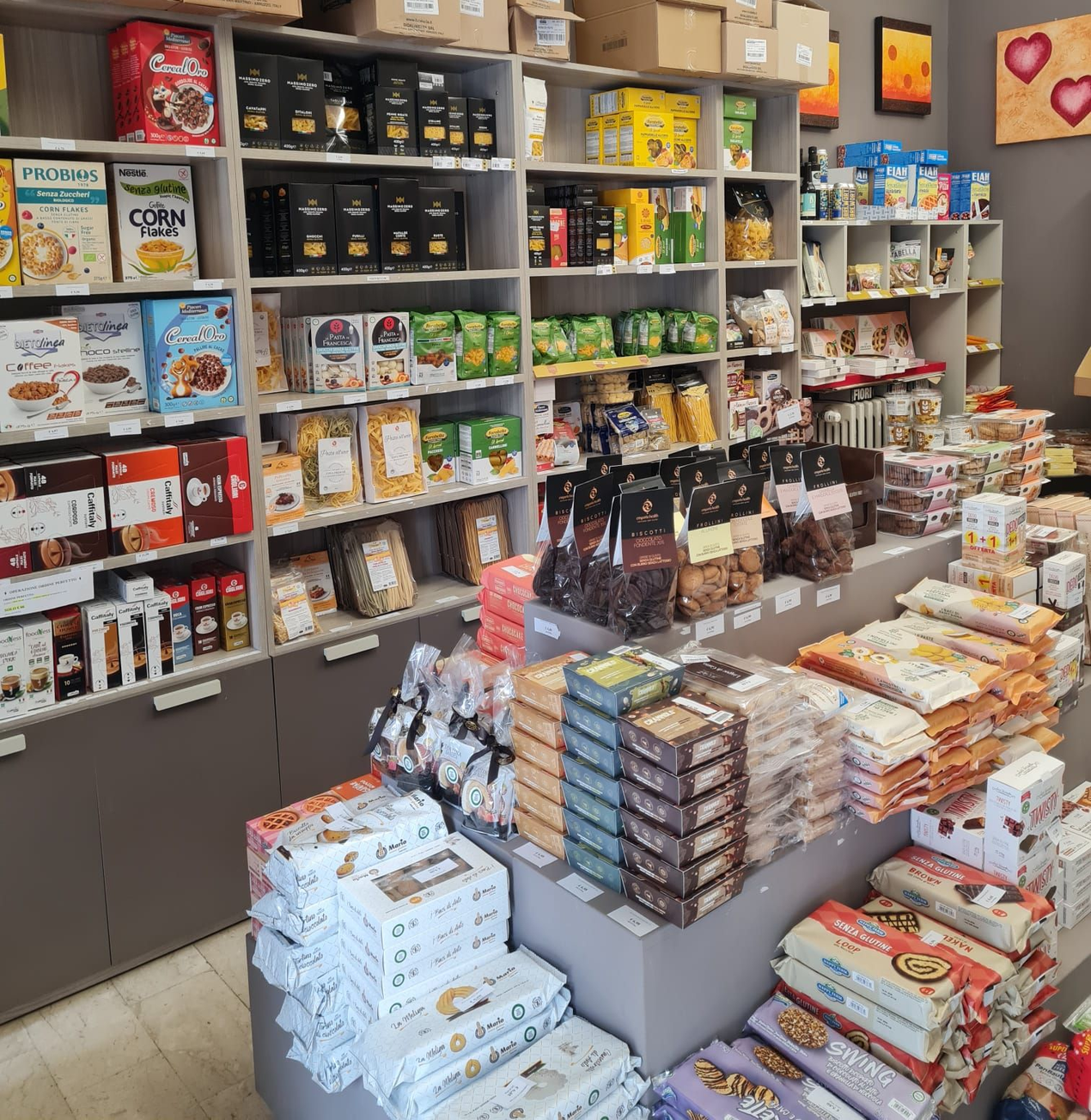 In un piccolo negozio, scaffali e tavoli pieni di snack e bevande confezionati di vario genere.