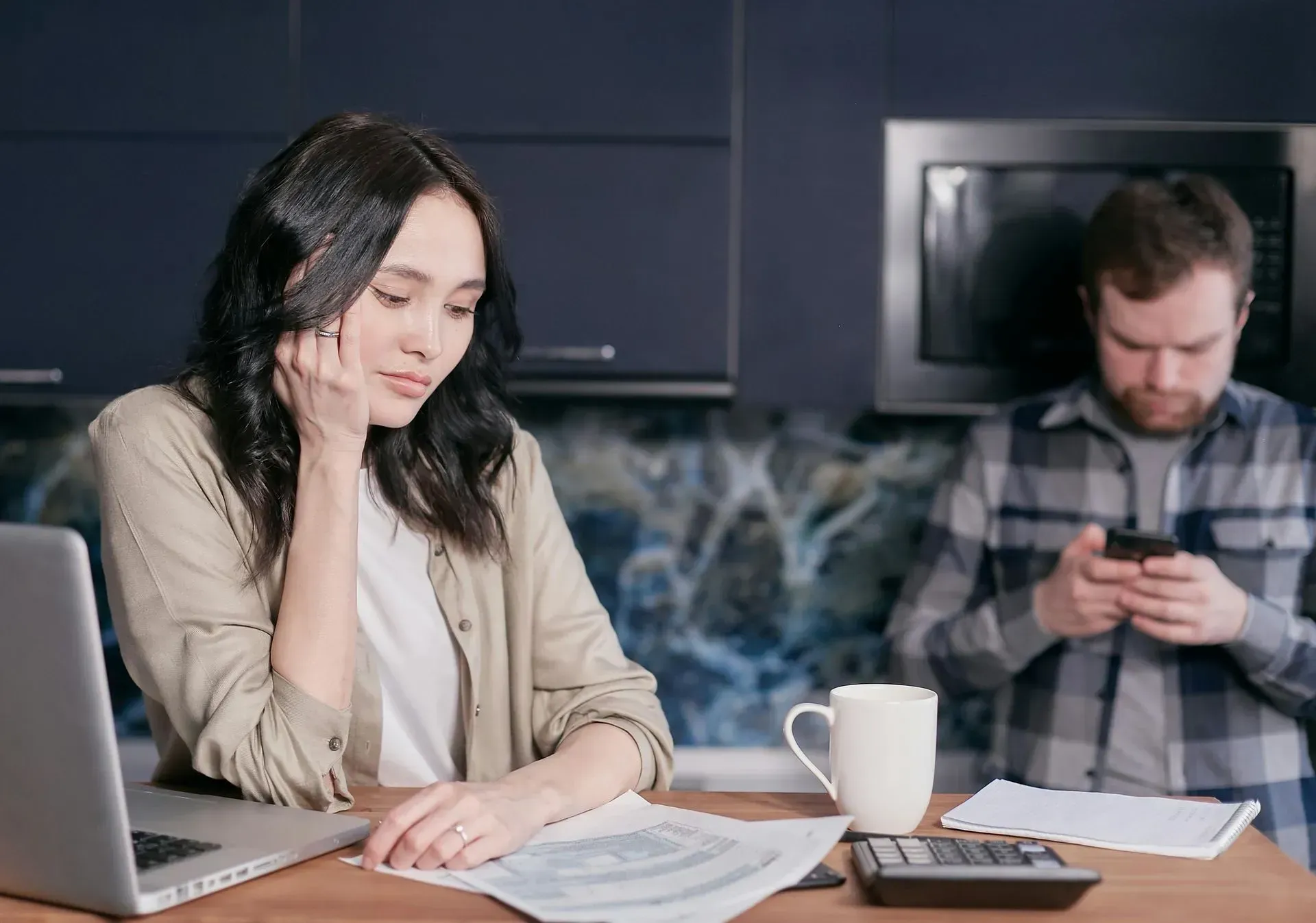 a woman is sitting at a table with a laptop and a man is using a cell phone
