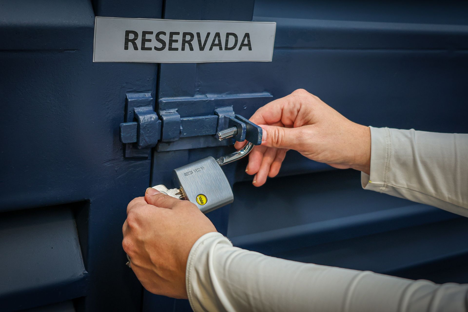 Manos abriendo un candado en una puerta de metal azul con la etiqueta 