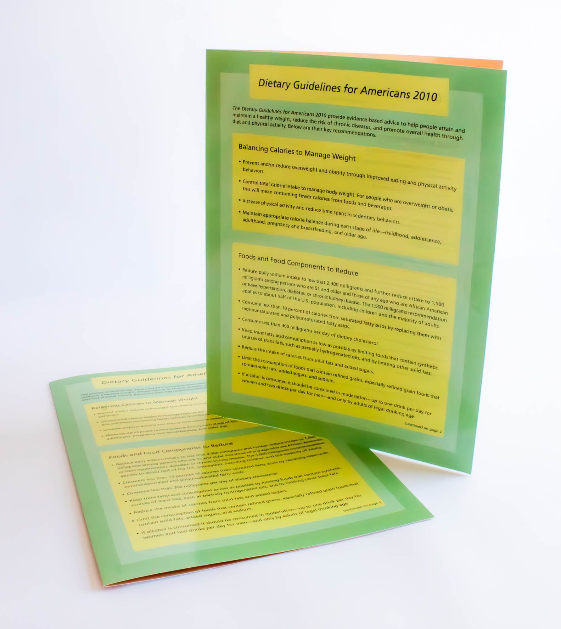 Green brochure with yellow text, leaning against another brochure on a white surface.