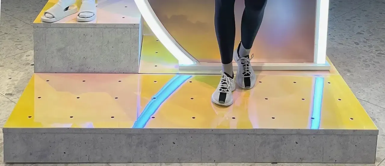 Person in black leggings and sneakers walking on a yellow and blue lit stage.