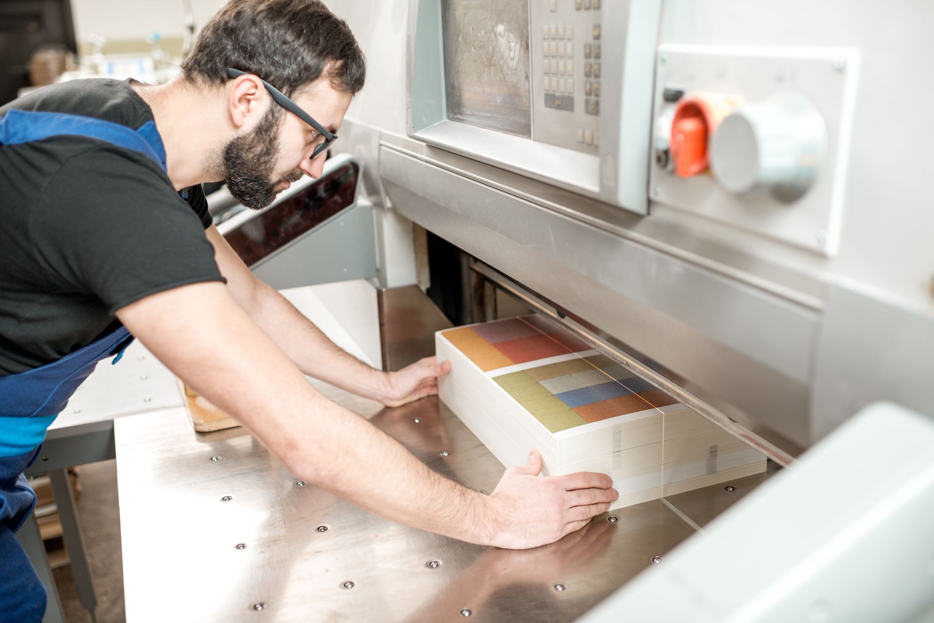 Man using a paper cutter machine to trim a stack of printed materials.