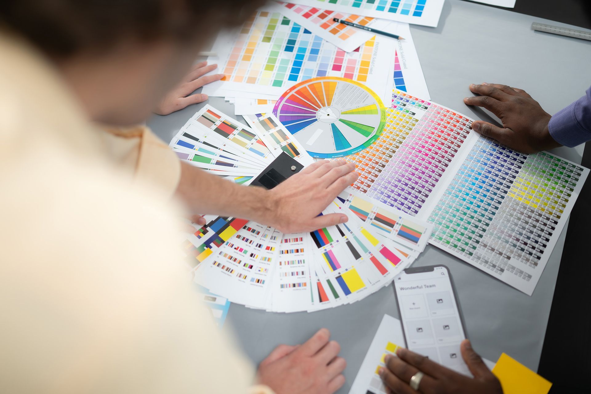 Hands pointing at color swatches and a color wheel, discussing design.