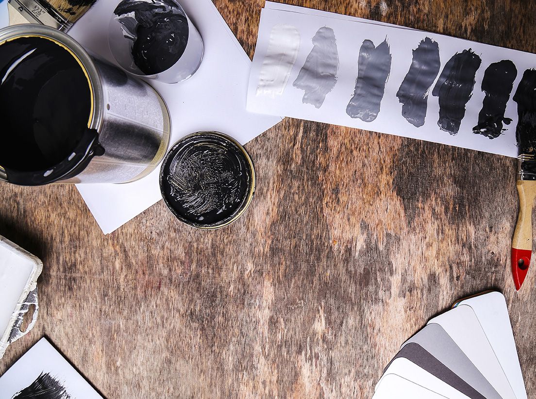 Paint cans, swatches of grey paint colors, and a paintbrush on a wooden surface.