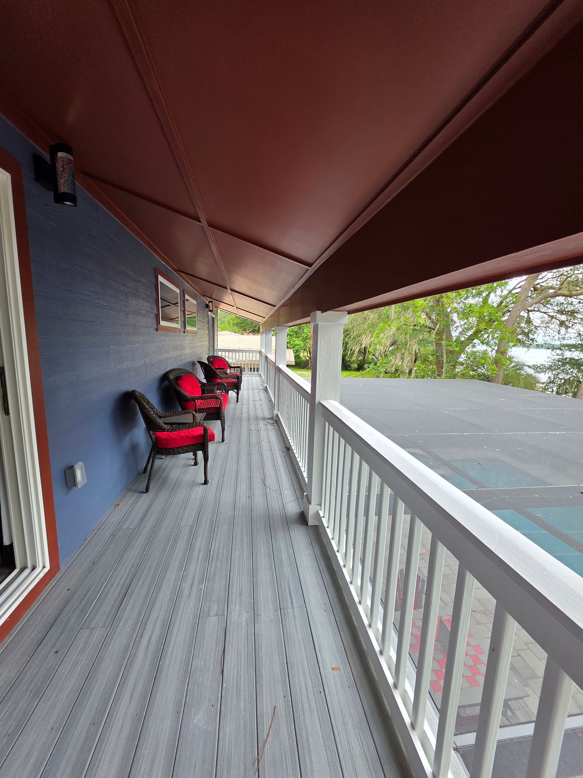Long porch with gray floor, white railing, red chairs, and blue wall.