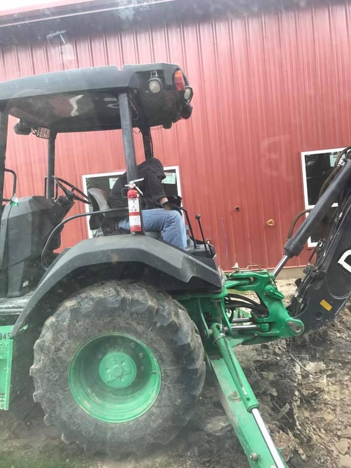 A man is driving a green tractor in front of a red barn.
