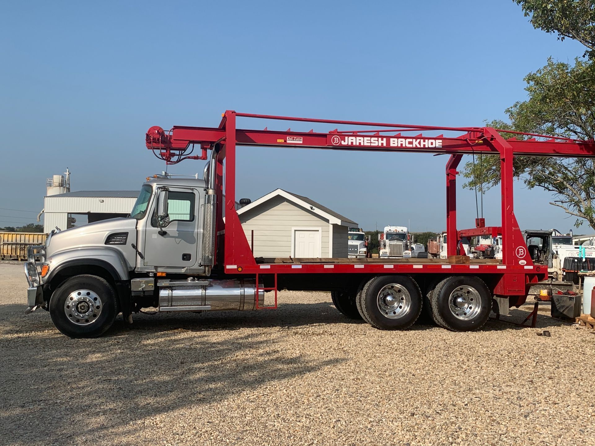 A red truck with a crane on the back is parked in a gravel lot.