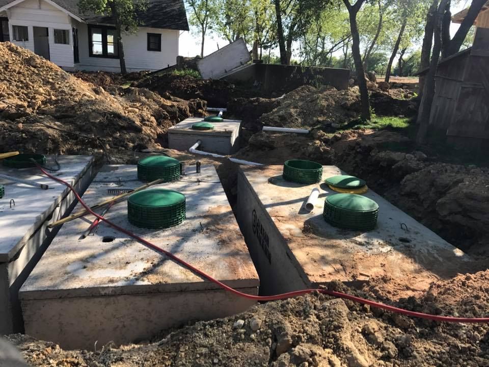 A septic tank is being built in the dirt in front of a house.