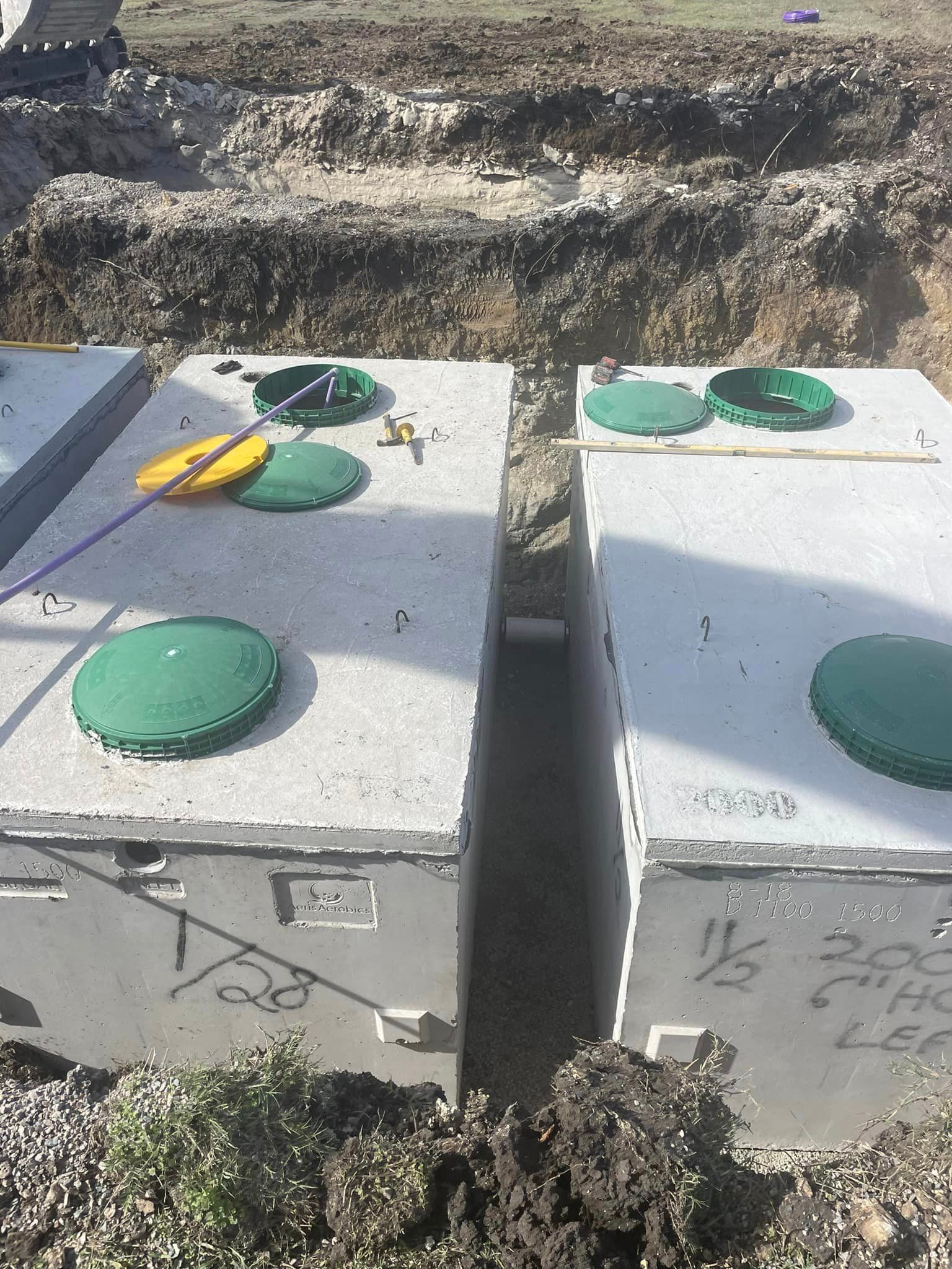 Two concrete septic tanks are sitting next to each other in a dirt field.
