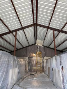 Plastic-covered interior of a warehouse under construction, with a ladder centered at the back.