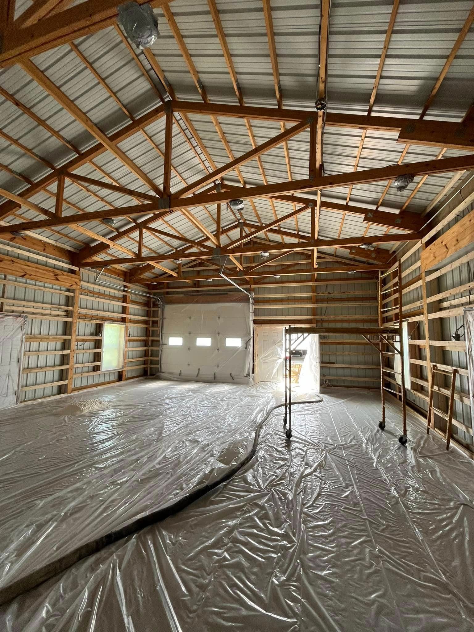 Interior of a large unfinished building with wooden beams, metal roof, and plastic sheeting covering the floor.