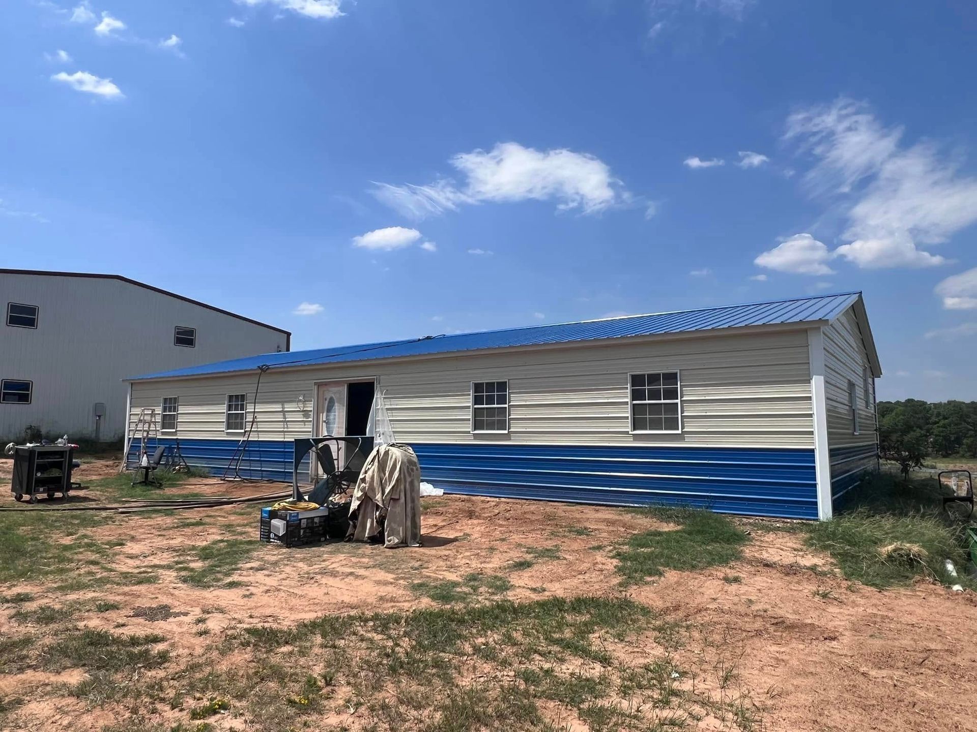 Blue and white metal building on a dirt lot, under a blue sky.