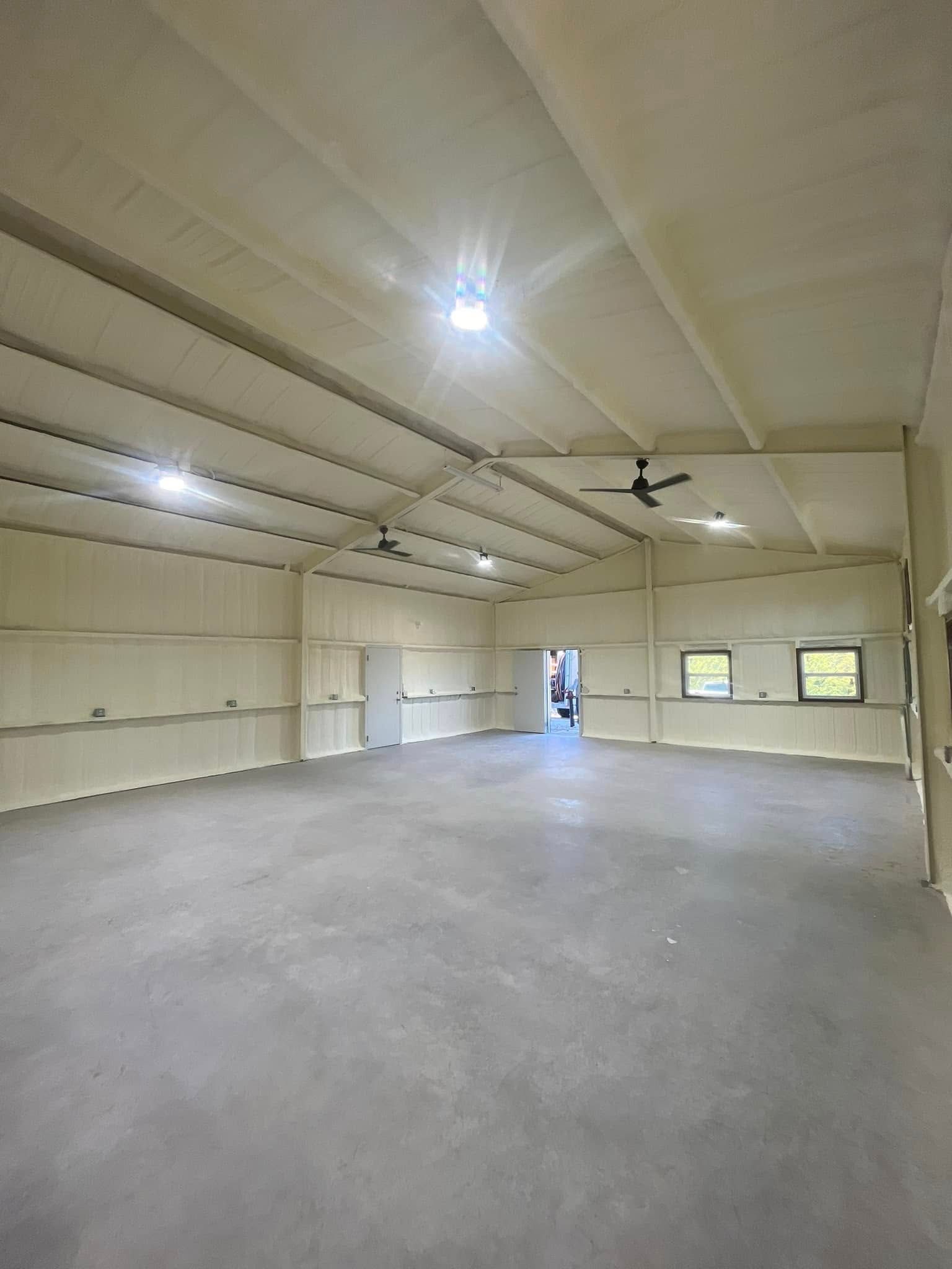 Interior of a large, empty commercial space with concrete floor, metal walls, and ceiling with lighting and fans.