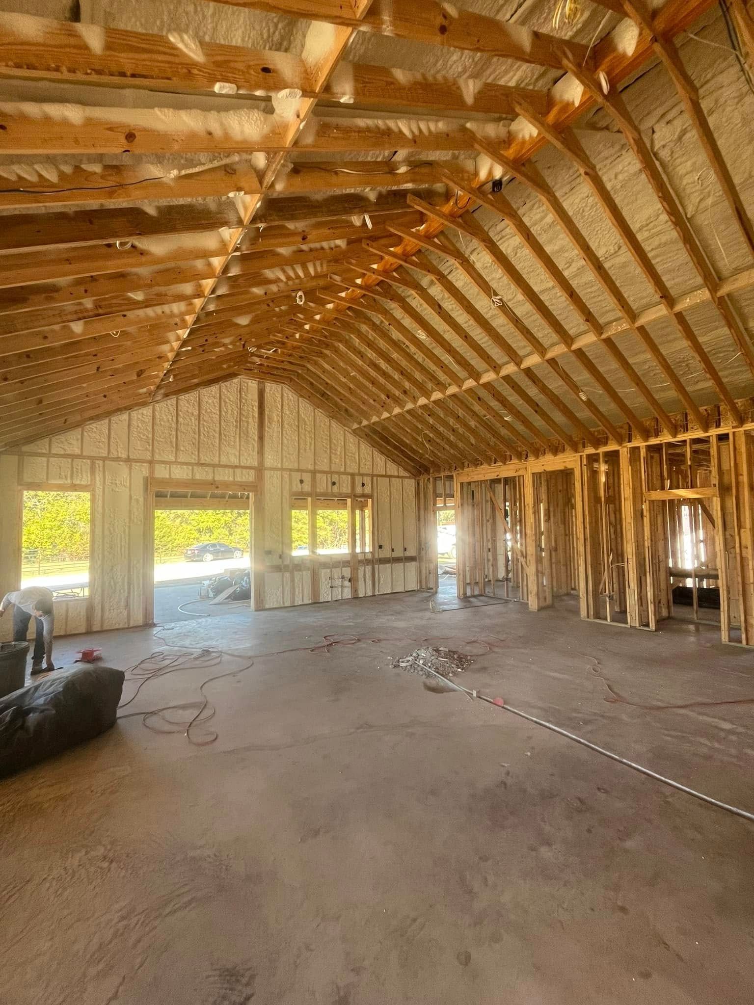 Interior of a building under construction, showing exposed wooden beams, insulation, and concrete floor.