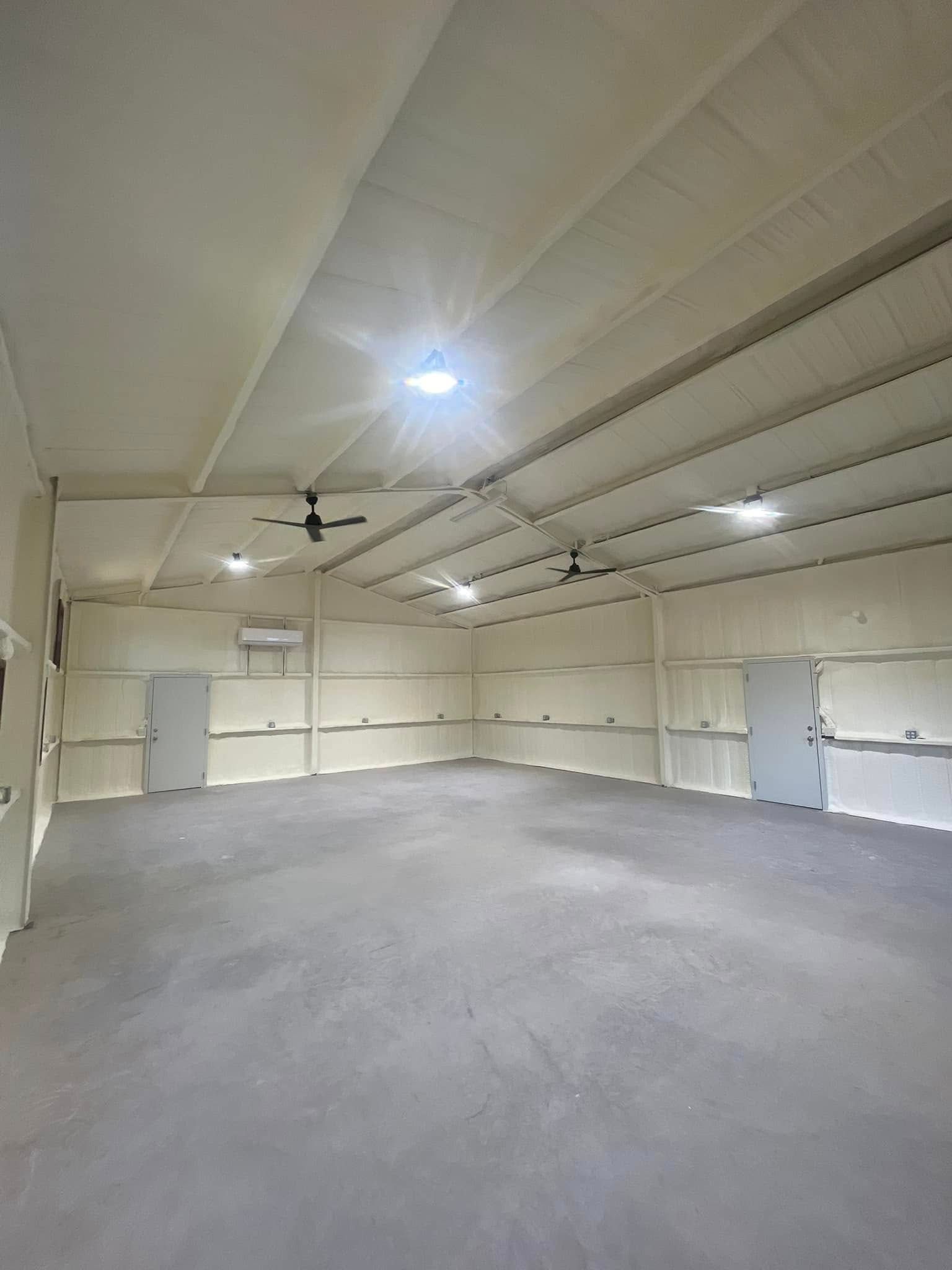 Interior view of a large, empty, white-walled room with a gray floor, several doors, and ceiling fans.