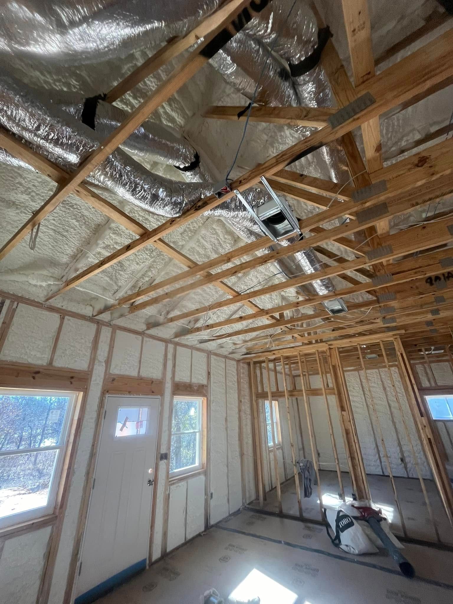Interior of a room under construction, with wood framing and spray foam insulation visible.