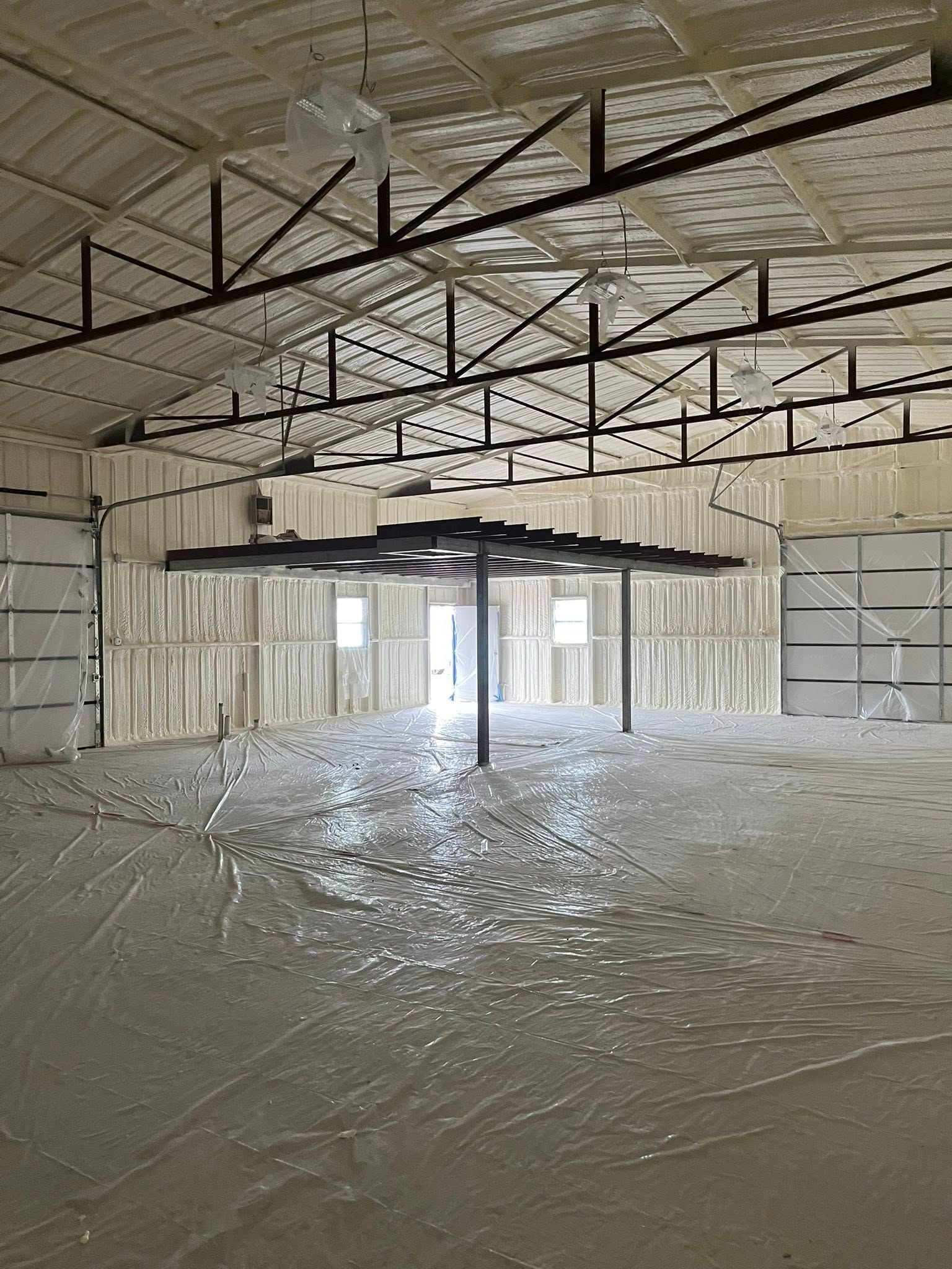 Interior of a building with spray foam insulation on walls and ceiling. Concrete floor. Metal support structure in the center.