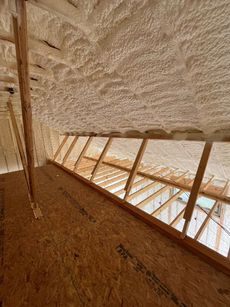 Interior of a wooden structure with a slanted thatched roof and bright window openings along one side