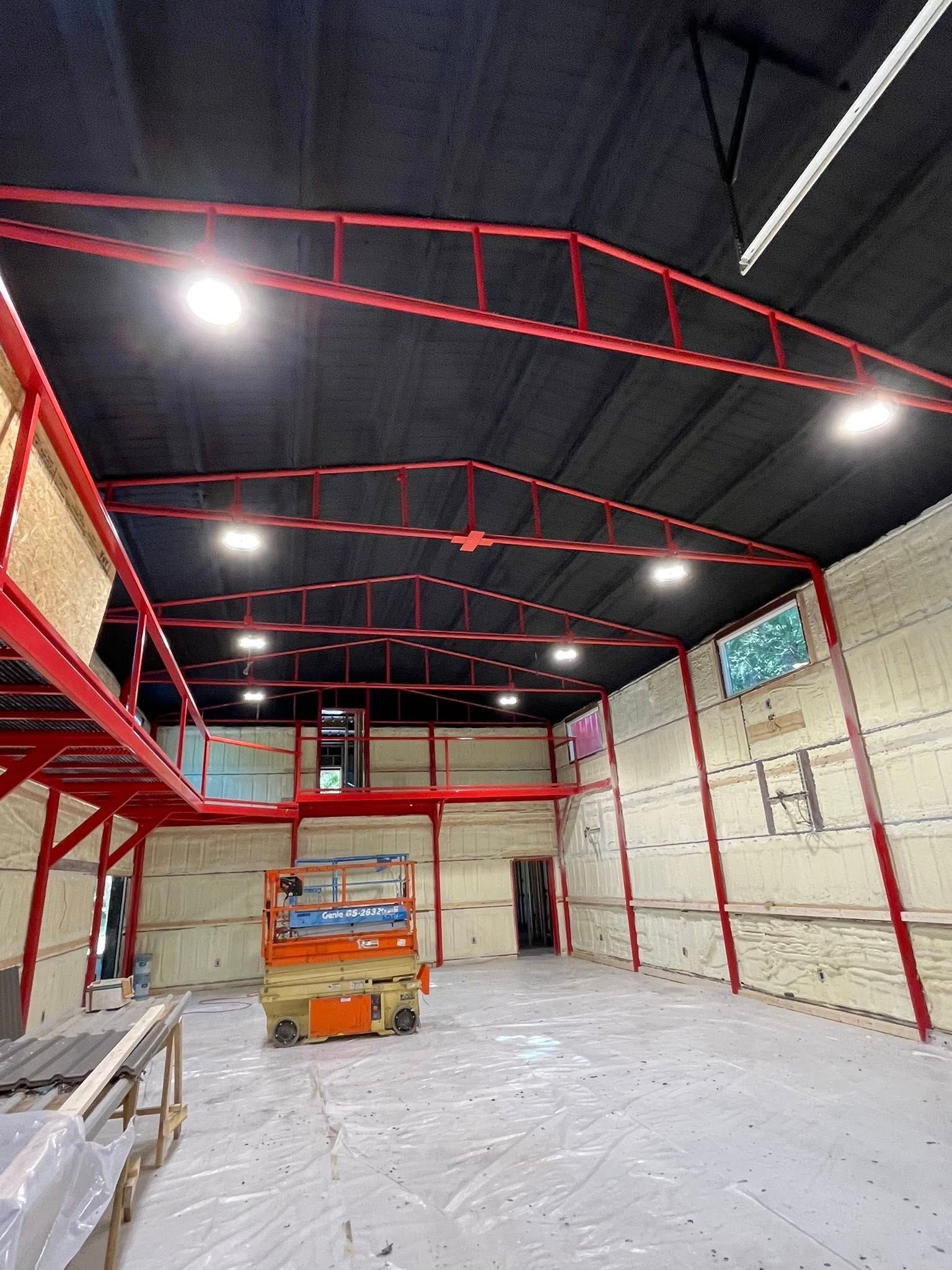 Interior view of a warehouse with red steel beams, black ceiling, bright lights, and an orange lift.