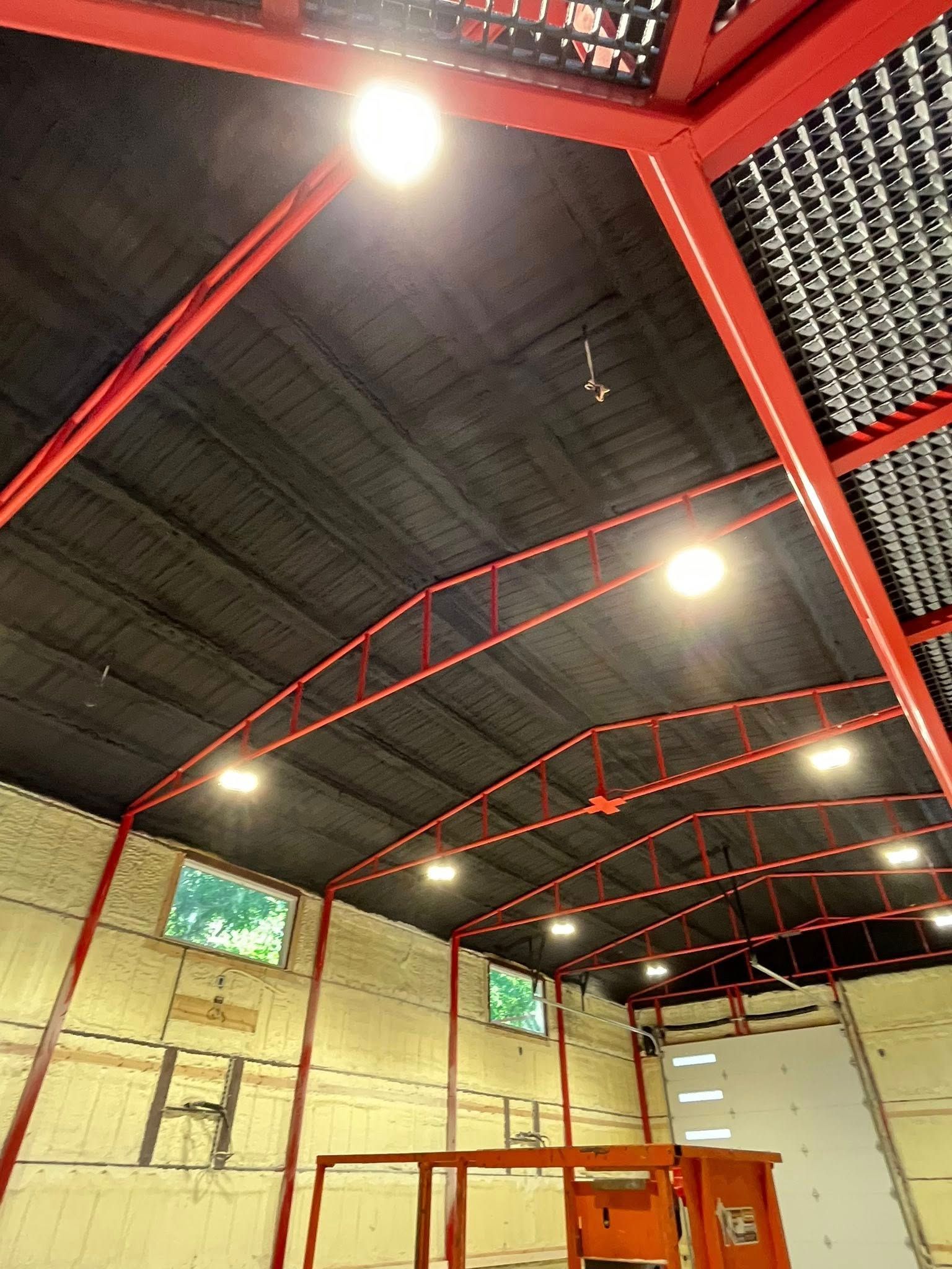 Interior of a building with red metal framework, dark ceiling, and bright overhead lights.