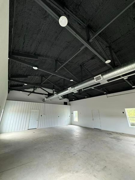 Empty, open room with black ceiling, white walls, and concrete floor.