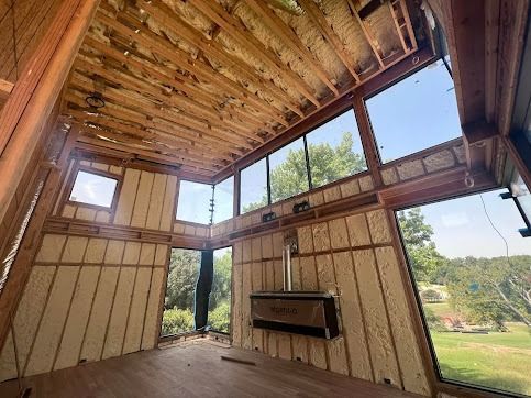 Interior view of a building under construction, featuring wooden framing, insulated walls, and large windows with an outdoor view.