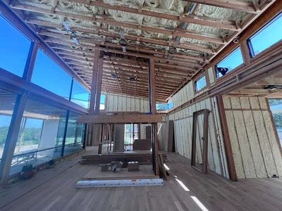 Interior of a renovated room with exposed ceiling beams, large windows, and unfinished wood walls