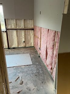 Partially insulated room with exposed pink wall insulation and debris on the floor