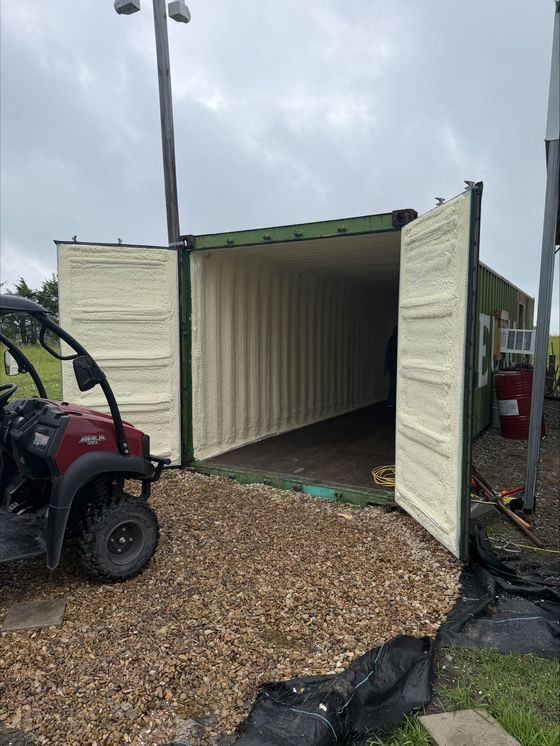 Open shipping container with white interior beside a red ATV on a gravel lot