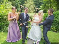 Wedding party playfully tugging mallets. Bride, groom, and attendants on lawn, greenery. Wedding Games 
